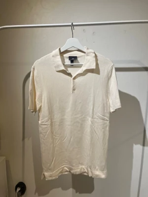 Vit pikétröja - Säljer en stilren beige polotopp från H&M i storlek S. Tröjan har korta ärmar, klassisk krage och knäppning framtill. Tillverkad i mjuk bomull som känns skön mot huden. Perfekt för dig som gillar en enkel men snygg look.