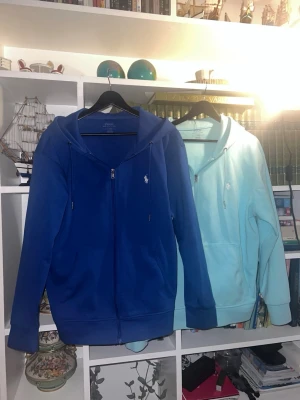 Blå hoodie från Polo Ralph Lauren - Två snygga hoodies från Polo Ralph Lauren med dragkedja framtill, huva med dragsko och två fickor. Ikoniska vita loggan broderad på bröstet. Tillverkad i mjuk bomullsblandning som är skön att ha på sig. Perfekt för en avslappnad och stilren look. Kan tänka mig släppa båda samtidigt för 800kr, om ni bara är sugen på en utav dom så kan vi diskutera pris :)
