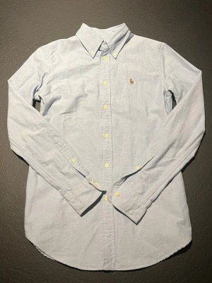 Ralph Lauren skjorta - En riktigt fin ljusblå skjorta ifrån Ralph Lauren i modellen Oxford och i storlek XS custom fit så var helst helt säker på att det är din storlek innan du köper! Kvaliteten är extremt fin och jag skulle ge den en 9/10, den har inga skavanker eller tecken på användning vad jag ser! 👌Skriv gärna om du vill ha fler bilder på plagget!📸 Tveka inte på att fråga vid minsta fundering!🖋️ Fraktar alltid senast dagen efter beställning!📦100% bomull