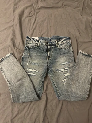 Ljusblå slitna skinny jeans - Säljer ett par ljusblå skinny jeans med slitningar och distressed detaljer framtill. Jeansen har klassisk femficksmodell, bälteshällor och dragkedjegylf. Perfekta för en avslappnad och trendig look.