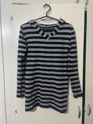 Randig hoodie i marinblått och grått - Snygg hoodie med marinblå och grå horisontella ränder. Långärmad med huva och V-ringad hals. Mjuk och bekväm, perfekt för chill dagar. Materialet känns som bomullsmix. Inga hål eller fläckar. Den är lite glittrig. Passar till höst och vinter.