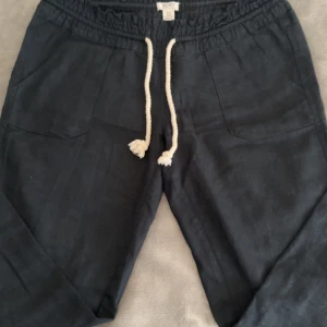 Svarta linne byxor från Roxy - Snygga svarta byxor från Roxy med elastisk midja och vit snörning. Byxorna har praktiska fickor både fram och bak, samt en diskret broderad logga på bakfickan. Perfekta för en avslappnad stil. Ganska Low waist och är helt nya, utan några skador. Har inte kunnat avändt dessa byxor på grund av att jag beställde i fel storlek. Kontakta för mer info.💞
