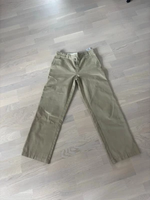 Beige Dickies 874 chinos - Säljer ett par klassiska beige Dickies 874 chinos med rak passform och hög midja. Byxorna har hällor för skärp, dragkedjegylf och är tillverkade i ett slitstarkt bomulls- och polyesterblandat material. Perfekta för en clean och avslappnad stil.