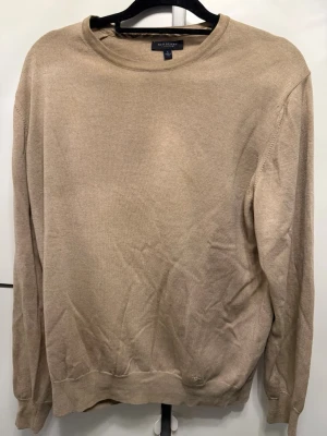 Beige Kashmir  tröja från burbbery london - En stilren beige tröja från burberry med rund halsringning och långa ärmar. Tröjan har ribbade muddar vid ärmslut och nederkant, vilket ger en klassisk look. Perfekt att matcha med jeans eller chinos för en clean outfit.