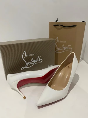 Vita pumps från Christian Louboutin - Säljer ett par klassiska vita pumps från Christian Louboutin med spetsig tå och den ikoniska röda sulan. Skorna har en elegant smal klack och är tillverkade i glansigt läder. Perfekta för dig som vill ha en tidlös och lyxig look.