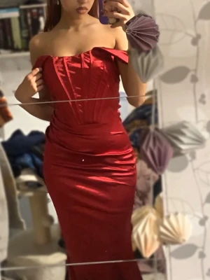 Balklänning- Ny! - Snygg röd balklänning med offshoulder-design och figurnära passform. Klänningen har en glansig finish och markerad midja, vilket ger en elegant siluett. Perfekt för dig som vill sticka ut med en klassisk och trendig look. Aldrig använd!!