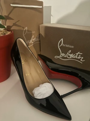 Svarta lackpumps från Christian Louboutin - Snygga svarta pumps i lack från Christian Louboutin med klassisk spetsig tå och ikonisk röd sula. Skorna har hög klack och elegant form, perfekta för att lyfta vilken outfit som helst. Märkeslogga i guld på insidan.