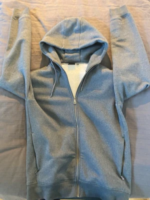 Grå zip-hoodie med huva - Sail Racing hoodie i grått, modell SR Zip Hood. Aldrig använd, så den är i nyskick utan slitage eller fläckar. Väldigt mjuk och skön med fleecefodrad insida och dragkedja framtill. Storlek L