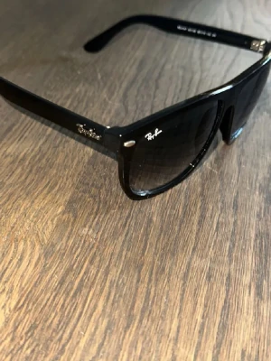 Rayban boyfriend  - Klassiska mörkblå  solglasögon från Ray-Ban med bred båge och ikonisk logga på sidan. Snygg, tidlös design med mörka glas och diskreta silvriga detaljer vid fronten. Perfekta för soliga dagar och ger en cool vibe till din outfit.