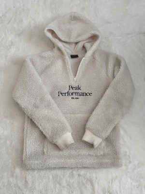 Vit teddyhoodie från Peak Performance - Mysig vit teddyhoodie från Peak Performance med halv dragkedja och broderad logga på bröstet. Hoodien har känguruficka och ribbade muddar vid ärmslut. Storlek 160, passar mig som i vanliga fall bär xs💕