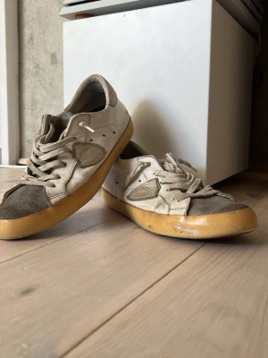 Ett par snygga philippe model skor - Snygg philipp model skor som är silverfärgade och vita dom är inte i det bästa skicket. skorna har utbytta sulor och lite upprivet material vid hälen.