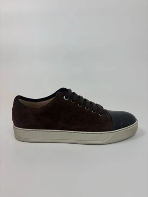 Bruna Lanvin sneakers med mocka och läderdetalj - Snygga bruna sneakers med ovandel i mocka och svart läderdetalj med krokopräglad struktur på tån. Skorna har vita sulor och bruna skosnören. Perfekta för dig som gillar en stilren men unik look.