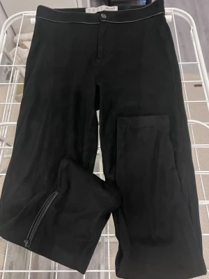 Svarta leggings med dragkedja från Denim&Co - Snygga svarta leggings från Denim&Co i mjukt material med dragkedjor vid bensluten. Hög midja och smal passform som sitter tajt längs benen. Perfekta att styla med oversized tröjor eller hoodies.