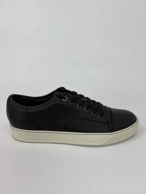Svarta Lanvin sneakers med vit sula - Stilrena svarta sneakers i läder med vit, tjock sula och svarta skosnören. Skorna har en klassisk låg profil och rundad tå, samt metallöljetter för snörningen. Perfekta för en clean och modern look.