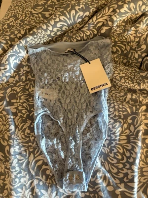 Ljusblå spetsbody från Bershka - Säljer en ljusblå body i spets från Bershka. Bodyn har högt skuren benlinning, tryckknappar i grenen och är helt i transparent spets med blommönster. Perfekt för dig som gillar trendiga och feminina underkläder.