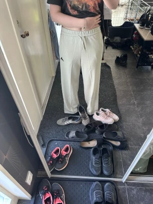Beige Adidas mjukisbyxor med ränder - Säljer ett par beige mjukisbyxor från Adidas med coola mönstrade ränder längs sidorna och logga framtill. Byxorna har resår i midjan och raka ben för en avslappnad look. Perfekta för chill dagar eller träning. Väldigt skönt matrial