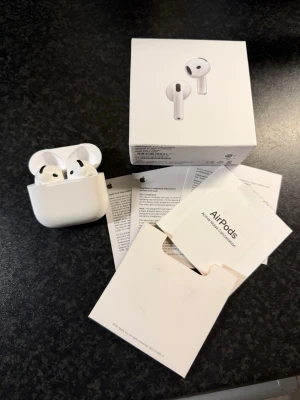 AirPods 4 - Säljer ett par Apple AirPods med trådlöst laddningsetui. Hörlurarna är vita och har en stilren, minimalistisk design i hård plast. Kommer med originalförpackning och manualer. Perfekta för musik, samtal och vardagslyssning.