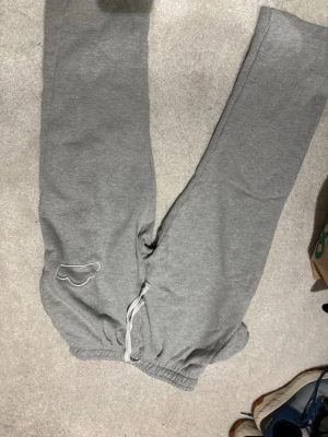Grå mjukisbyxor från Hats-On , strl S - Grå mjukisbyxor från Hats-on med elastisk midja och dragsko. Byxorna har en broderad moln-detalj på ena benet och är tillverkade i mjukt bomullsmaterial. Perfekta för chill dagar hemma eller när du vill vara extra bekväm. 