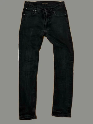 Svarta slim fit jeans från Nudie Jeans - Svarta slim fit jeans från Nudie Jeans med klassisk femficksdesign och diskreta sömmar. Jeansen har en smal passform och är tillverkade i stretchigt denim för extra komfort. Perfekta för en stilren och modern look.         Kan gå ner i pris vid snabb och smidig affär!