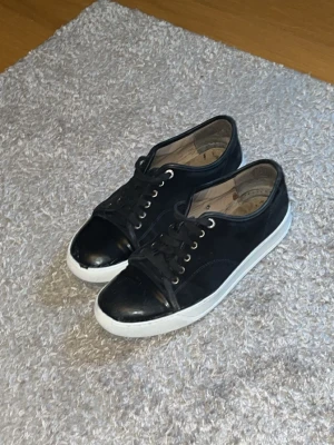 Lanvins - Snygga svarta lanvins med lågt skaft och vit sula. Skorna har svarta skosnören, metallfärgade öljetter och en stilren design. Perfekta för en clean och klassisk look. Bytt innersula i skorna också. Skriv för mer info
