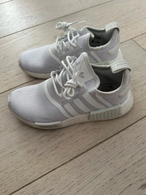Vita Adidas NMD_R1 sneakers - Fräscha vita Adidas NMD_R1 sneakers med klassiska tre ränder på sidan. Ovandelen är i meshmaterial som andas och sulan är i gummi med boost-dämpning för extra komfort. Endast använda ett fåral gånger inomhus på gymmet
