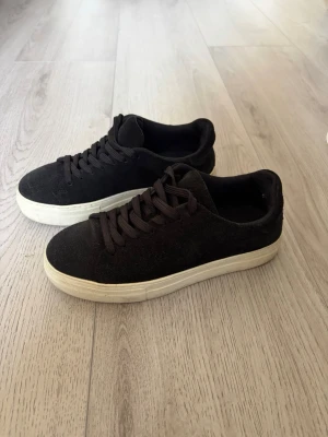 Svarta sneakers från Selected Homme - Stilrena svarta sneakers med tjock vit sula och ovandel i mockaliknande material. Klassisk låg modell med svarta skosnören och enkel design som passar till det mesta. Perfekta för dig som gillar en clean och tidlös look.
