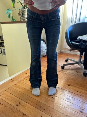 Mörkblå lågmidjade bootcut jeans från Lee - Snygga mörkblå low waist bootcut jeans från Lee med klassisk femficksdesign och dubbla knappar i midjan. Jeansen har lätt slitna detaljer för en cool vintage look. Storlek W29 L33. Godkänner prisförslag vid snabb affär!💕