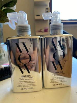 Color Wow Dream Coat Supernatural Spray - Två flaskor Color Wow Dream Coat Supernatural Spray, 200 ml vardera. Sprayen har en silvrig, spegelblank rektangulär flaska med svart text och pumpfunktion. Produkten används för att ge håret glans, skydd mot fukt och en slät finish.