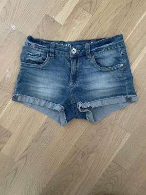 Blå jeansshorts från LAB Industries - Snygga blå jeansshorts från LAB Industries med råa kanter och klassisk femficksdesign. Shortsen har knapp och dragkedja framtill samt bälteshällor. Tillverkade i bomull och perfekt för sommaren.