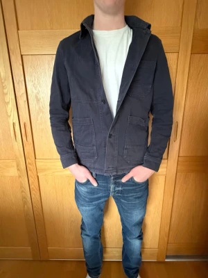 Mörkblå overshirt med fickor - Stilren mörkblå overshirt med två stora bröstfickor och knäppning framtill. Jackan har en avslappnad passform och är tillverkad i bomull. Storlek 46 för arket men motsvar ungefär en small. Pris går att diskutera