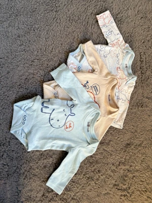 Söta bodys med djurmotiv från So Cute - Tre långärmade bodys från So Cute i mjuk bomull. En ljusblå med flodhästtryck, en beige med valmotiv och texten 'Happy Friends', samt en vit med färgglada djurkonturer. Perfekta för mysiga dagar och lek. Alla har praktiska tryckknappar i grenen. En oanvänd och dom andra två minimal används