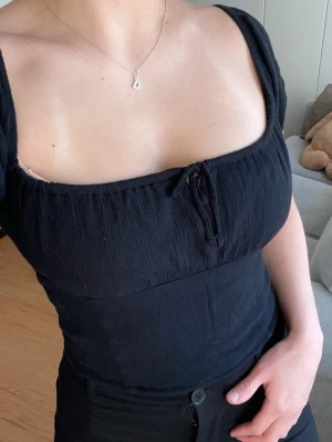 Svart topp Hollister - Svart blus med fyrkantig ringning, korta puffärmar och knyt framtill. Toppen är figurnära. 