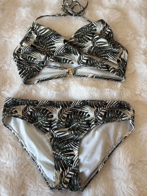 Vit bikini med palmbladsmönster - Snygg bikini med svart och grönt palmbladsmönster på vit botten. Överdelen har omlott-design och knyt i nacken samt spänne bak. Underdelen är klassisk med samma mönster. Skriv för frågor❤️