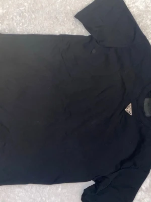 Svart t-shirt från Prada - Snygg svart t-shirt från Prada med klassisk passform och diskret logga på bröstet. Tillverkad i mjuk bomull som känns skön mot huden. Perfekt för dig som gillar stilrena och exklusiva plagg med en lyxig touch.
