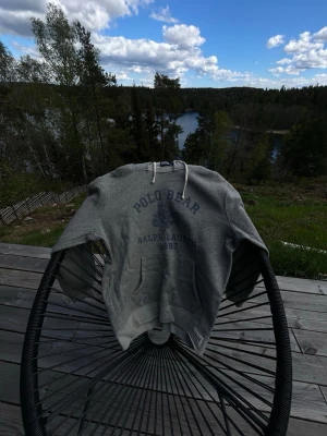 Ralph Lauren hoodie - Snygg grå hoodie från Ralph Lauren med Polo Bear-tryck och text framtill. Klassisk känguruficka, dragsko i huvan och mjukt material. Perfekt för en chill och avslappnad stil.
