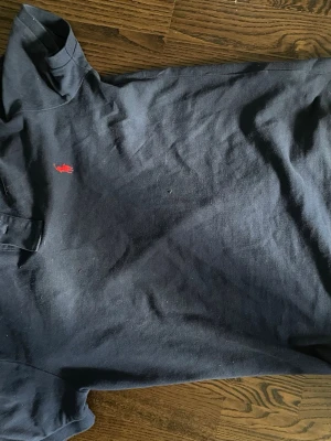 Mörkblå pikétröja från Polo Ralph Lauren - Klassisk mörkblå pikétröja från Polo Ralph Lauren med röd broderad logga på bröstet. Tröjan har korta ärmar, krage och knappar framtill. Tillverkad i mjuk bomull och har en slim passform.