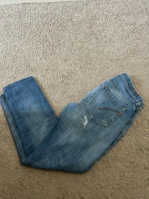 Blå raka jeans med slitningar - Säljer ett par klassiska blå jeans med raka ben och lätt slitna detaljer. Jeansen har fem fickor och synliga sömmar i kontrastfärg. Perfekta för en avslappnad och trendig look. Materialet är denim i bomull.