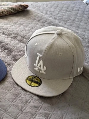 Grå LA-keps från New Era - Snygg grå keps från New Era med LA-logga framtill i vitt. Klassisk 59FIFTY-modell med platt skärm och broderad logga på sidan. Perfekt för dig som gillar streetwear och sportig stil.