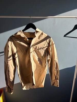 Beige bomullsskjorta i storlek S - Säljer en stilren beige skjorta från dressmann i storlek S. Skjortan är tillverkad i mjuk bomull och har klassisk krage, bröstficka och knäppning framtill. Perfekt för dig som gillar en enkel och clean look. Men även en vin röd båda 2!!!