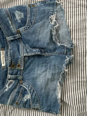  Lågmidjade Blåa jeansshorts med slitningar - Snygga blå jeansshorts från Replay med råa kanter och slitna detaljer. Klassisk femficksmodell med knappar framtill och mycket låg midja. Perfekta för varma dagar och en avslappnad stil. (Det saknas en knapp inne i byxorna men inget jag sj tänkt på) 💕 köpta på Vinted för 630kr. Skicka pris förslag godkänner de flesta💕