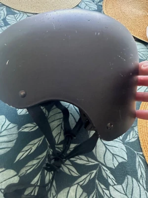 Svart hjälm med justerbart spänne 58-61 cm - Cool svart hjälm med rundad form och justerbart hakspänne. Utrustad med flera ventilationshål och vadderad insida för extra komfort. Perfekt för skate, cykel eller andra aktiviteter där du vill skydda huvudet.