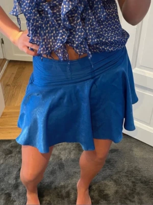 Blå glansig volang kortkjol Zara - Snygg blå kortkjol med glansigt tyg och mycket vidd. Kjolen har en bred linning och ett flowigt fall som ger en cool och ungdomlig look. Perfekt att styla med en topp eller skjorta för en trendig outfit.