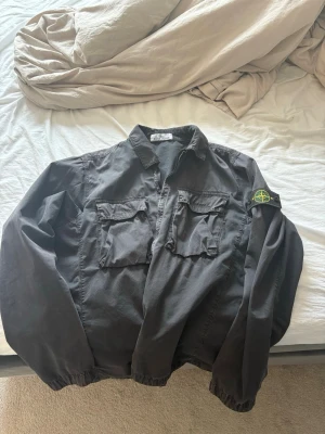 Svart overshirt från Stone Island - Snygg svart overshirt från Stone Island med klassisk patch på ärmen. Perfekt för lager-på-lager och streetwear-stil.