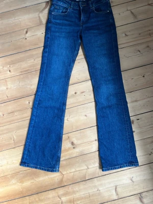 Blå bootcut jeans W25 L34 - Snygga blå bootcut jeans från från bikbok med klassisk femficksdesign och normalhög midja. Jeansen har en lätt utsvängd passform nertill och är tillverkade i ett slitstarkt denimtyg. Perfekta för en trendig och avslappnad look.  Nästan alldrig använda. 