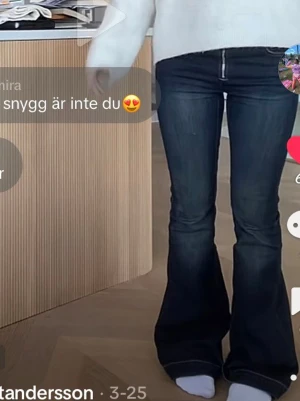 Mörkblå bootcut jeans med dragkedja - Säljer ett par mörkblå bootcut jeans med hög midja och en snygg, synlig dragkedja framtill. Jeansen har klassiska fem fickor och är tillverkade i stretchigt denimtyg som sitter tajt upptill och släpper ut vid benen. Perfekta för en trendig och avslappnad look.