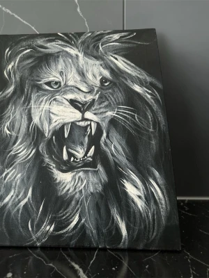 Svartvit tavla med lejonmotiv - Unik tavla med ett svartvitt motiv av ett rytande lejon. Målningen är gjord på canvas och har dramatiska penseldrag som framhäver lejonets man och uttryck. Perfekt för dig som vill ha en cool och kraftfull detalj till rummet. Köpt i afrika och gjord av konstnären Kano