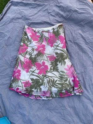 Blommig kjol från Cappuccini - Säljer en somrig blommig kjol från Cappuccini i vitt med rosa och gröna blommor och blad. 