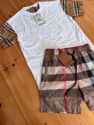  Burberry shorts t-shirt - Snygga shorts från Burberry med klassiskt rutigt mönster i bruna, svarta, beige och röda toner. Shortsen har elastisk midja med svart snörning och är perfekta för sommaren. Tillverkade i ett lätt och bekvämt material.