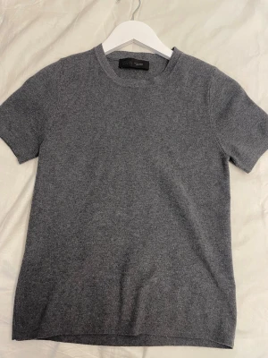 Grå stickad topp från ZARA - En stilren grå stickad topp från ZARA med rund halsringning och korta ärmar. Perfekt att matcha med jeans eller kjol för en enkel men snygg look. Mjuk och bekväm kvalitet som känns lyxig mot huden.