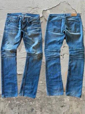Blå jeans från Acne Studios - Säljer ett par klassiska blå jeans från Acne Studios med snygg slitning och raka ben. Jeansen har fem fickor, gylf med dragkedja och läderpatch med logga bak i midjan. Perfekta för en avslappnad och trendig look. Obs en liten defekt, se sista bild. 